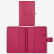 A pink leather planner or notebook cover shown closed and open on a light gray background. The closed view shows a strap closure with a small metal rivet, and the open view reveals interior pockets, a zipper compartment, and a small loop tab.
